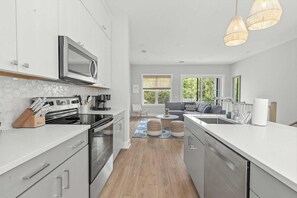 A modern kitchen with white cabinetry, a built-in microwave, and a large window. - Sincerely Shem II- 7 min to Beach and Dtwn CHS (Mount Pleasant)