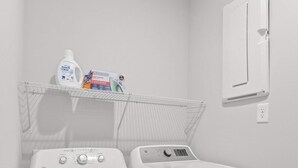 Een wasserette met twee witte wasmachines, een plank met schoonmaakmiddelen en een aan de muur bevestigde verwarming.