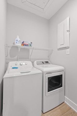 A laundry room with two white washing machines, a shelf with cleaning products, and a wall-mounted heater. - Sincerely Shem II- 7 min to Beach and Dtwn CHS (Mount Pleasant)