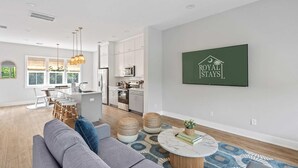 Een moderne woonkamer met een grijze bank, een salontafel en een eethoek met een witte tafel en stoelen.