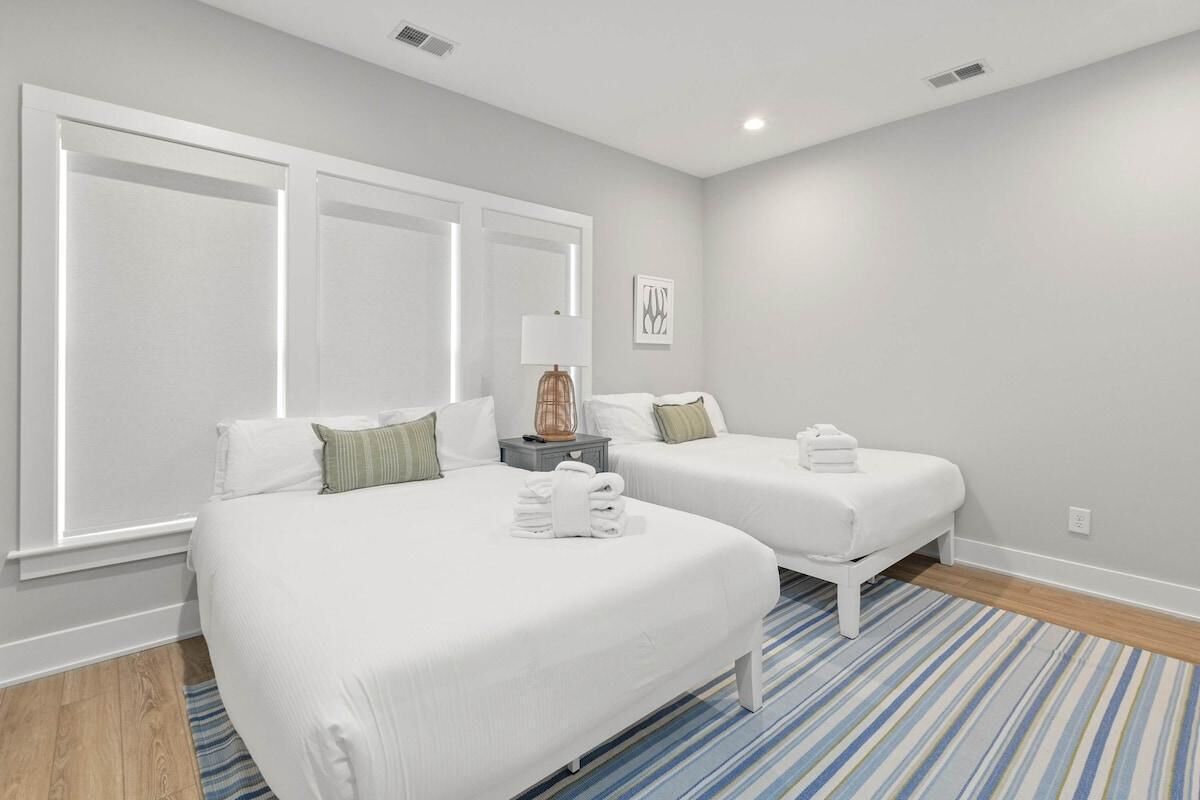 Habitación de hotel con una cama grande, dos camas más pequeñas, una mesita de noche con lámpara y una alfombra a rayas azules.