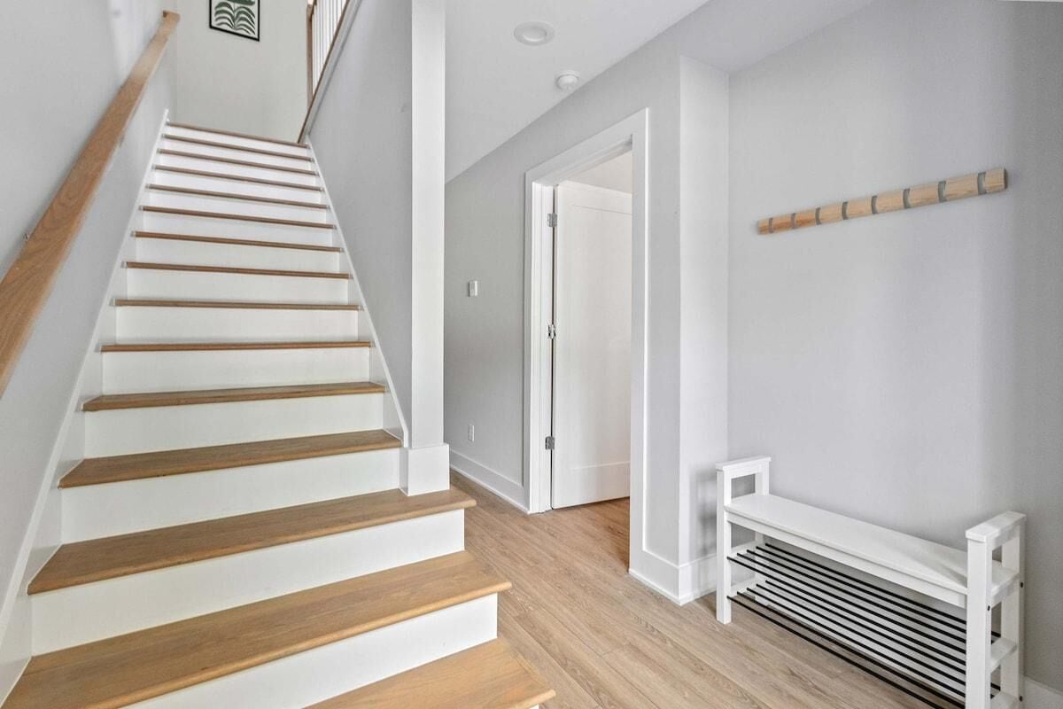 A staircase with wooden steps and white walls, leading to a room with a white bench and a wooden shelf.