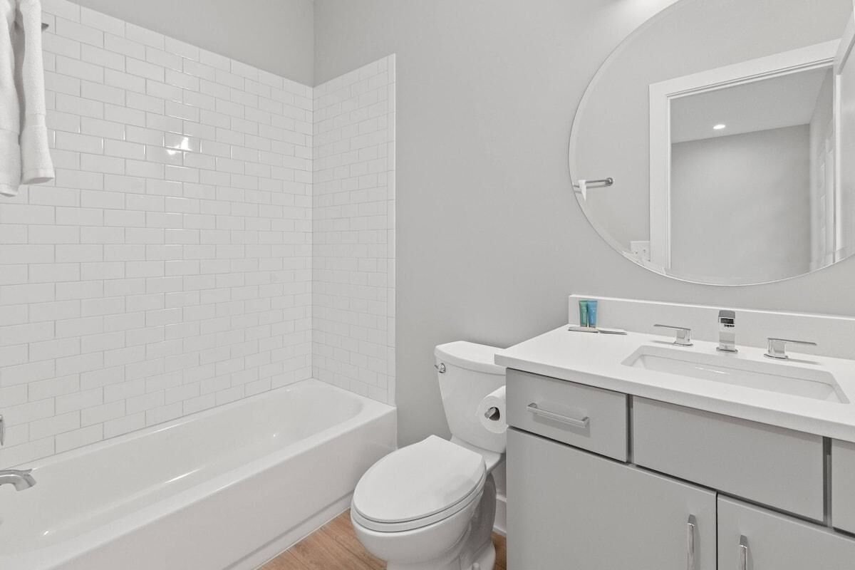 A modern bathroom with white tiles, a bathtub, a toilet, and a vanity with a mirror.