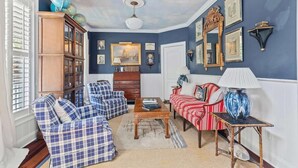 A living room with a blue wall, a wooden cabinet, a red sofa, a blue armchair, and a coffee table. - Boview Hall- Pool, Hot Tub-15 Mins to Kiawah (Johns Island)