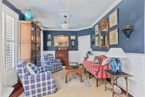 A living room with a blue wall, a wooden cabinet, a red sofa, a blue armchair, and a coffee table. - Boview Hall- Pool, Hot Tub-15 Mins to Kiawah (Johns Island)