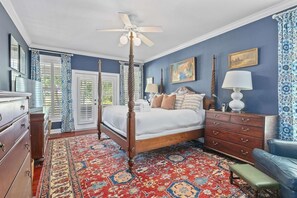 A bedroom with a four-poster bed, a ceiling fan, a large window with shutters, a patterned rug, and a dresser. - Boview Hall- Pool, Hot Tub-15 Mins to Kiawah (Johns Island)