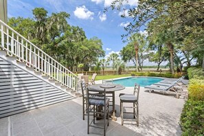 A pool area with a wooden deck, a table with chairs, and a view of the surrounding greenery and trees. - Boview Hall- Pool, Hot Tub-15 Mins to Kiawah (Johns Island)