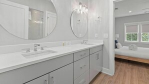 A modern bathroom with a double sink vanity, large mirrors, and a bench in the adjacent room. - Sincerely Shem Iii- 7 min to Beach and Dtwn CHS (Mount Pleasant)
