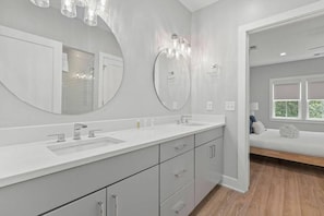 Ein modernes Badezimmer mit einem Doppelwaschtisch, großen Spiegeln und einer Bank im angrenzenden Raum.