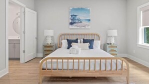 A bedroom with a wooden bed, white bedding, a beach-themed painting on the wall, and two bedside tables with lamps. - Sincerely Shem Iii- 7 min to Beach and Dtwn CHS (Mount Pleasant)