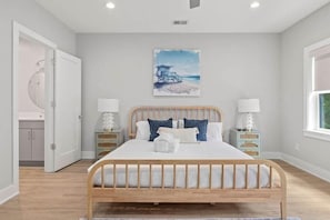 Ein Schlafzimmer mit einem hölzernen Bett, weißer Bettwäsche, einem Strandbild an der Wand und zwei Nachttischen mit Lampen.
