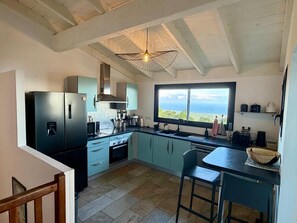 A kitchen with a view of the ocean, a modern stove, and a hanging light fixture. - "Kaz mer veille" Villa  (Les Avirons)