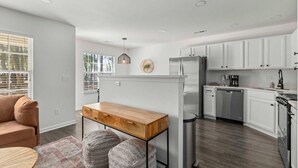 A modern kitchen with white cabinets, a wooden table, and a built-in refrigerator. - Boho Ferry- Mins From Credit One- Pet Friendly (Charleston)