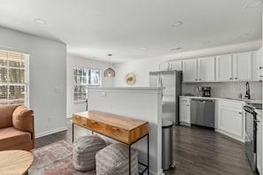 A modern kitchen with white cabinets, a wooden table, and a built-in refrigerator. - Boho Ferry- Mins From Credit One- Pet Friendly (Charleston)