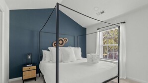 A bedroom with a four-poster bed, a nightstand, a window with curtains, and a decorative wall piece. - Boho Ferry- Mins From Credit One- Pet Friendly (Charleston)