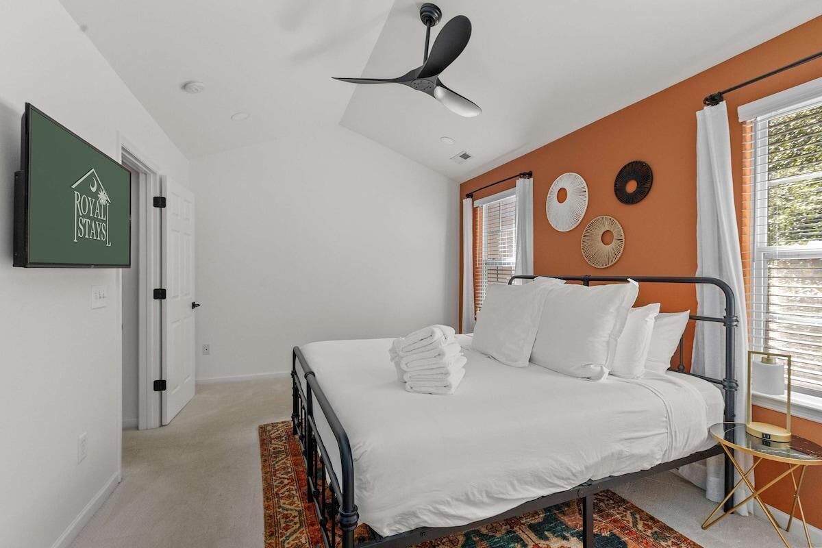 A bedroom with a bed, a ceiling fan, a wall-mounted TV, and a window with curtains.