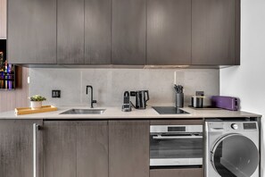 A modern kitchen with dark wood cabinets, a double sink, a coffee maker, a toaster, and a built-in oven and washer. - E11EVEN Studio · Bay Views + Rooftop Day Club Pool (Miami)