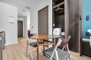 A modern hotel room with a dining area featuring a wooden table and chairs, a wardrobe with hanging clothes, and a visible control panel on the wall. - E11EVEN Studio · Bay Views + Rooftop Day Club Pool (Miami)