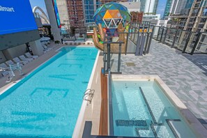 A swimming pool with a diving board and lounge chairs, surrounded by a tiled deck and modern buildings. - E11EVEN Studio · Bay Views + Rooftop Day Club Pool (Miami)