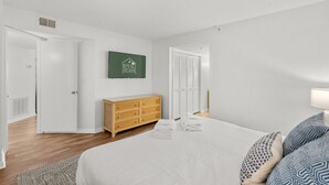 A hotel room with a bed, a wooden dresser, a wall-mounted sign, and a door leading to another room. - Beachfront Breeze @ Sea Castle North Myrtle Beach (North Myrtle Beach)