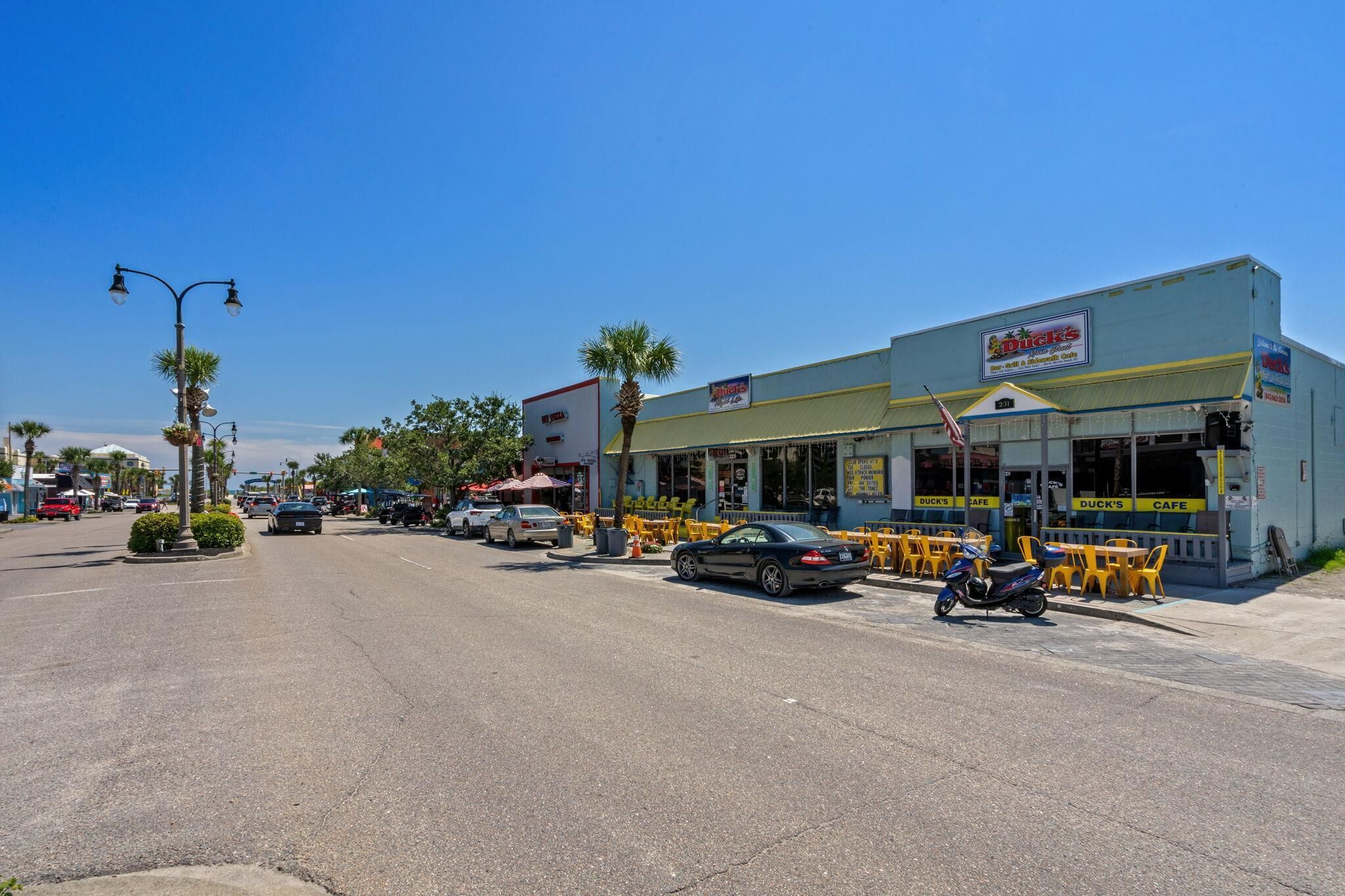 A street view with a building labeled 'Duck's Cafe' featuring outdoor seating and a parked motorcycle.