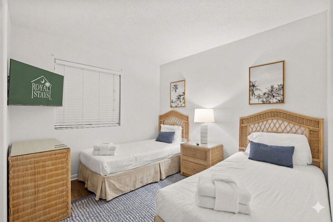 A hotel room with two single beds, a large bed, a TV, and a window with blinds.