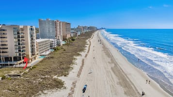 A coastal hotel with multiple floors, a sandy beach, and a clear blue sky.