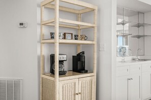 A corner shelf unit with coffee mugs and a coffee maker, a white wall, a vent, and a kitchen area with cabinets and a window. - Beachfront Breeze @ Sea Castle North Myrtle Beach (North Myrtle Beach)