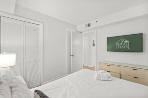 A hotel room with a bed, a TV mounted on the wall, a bedside table with a lamp, a wardrobe, and a bathroom door. - Beachfront Breeze @ Sea Castle North Myrtle Beach (North Myrtle Beach)