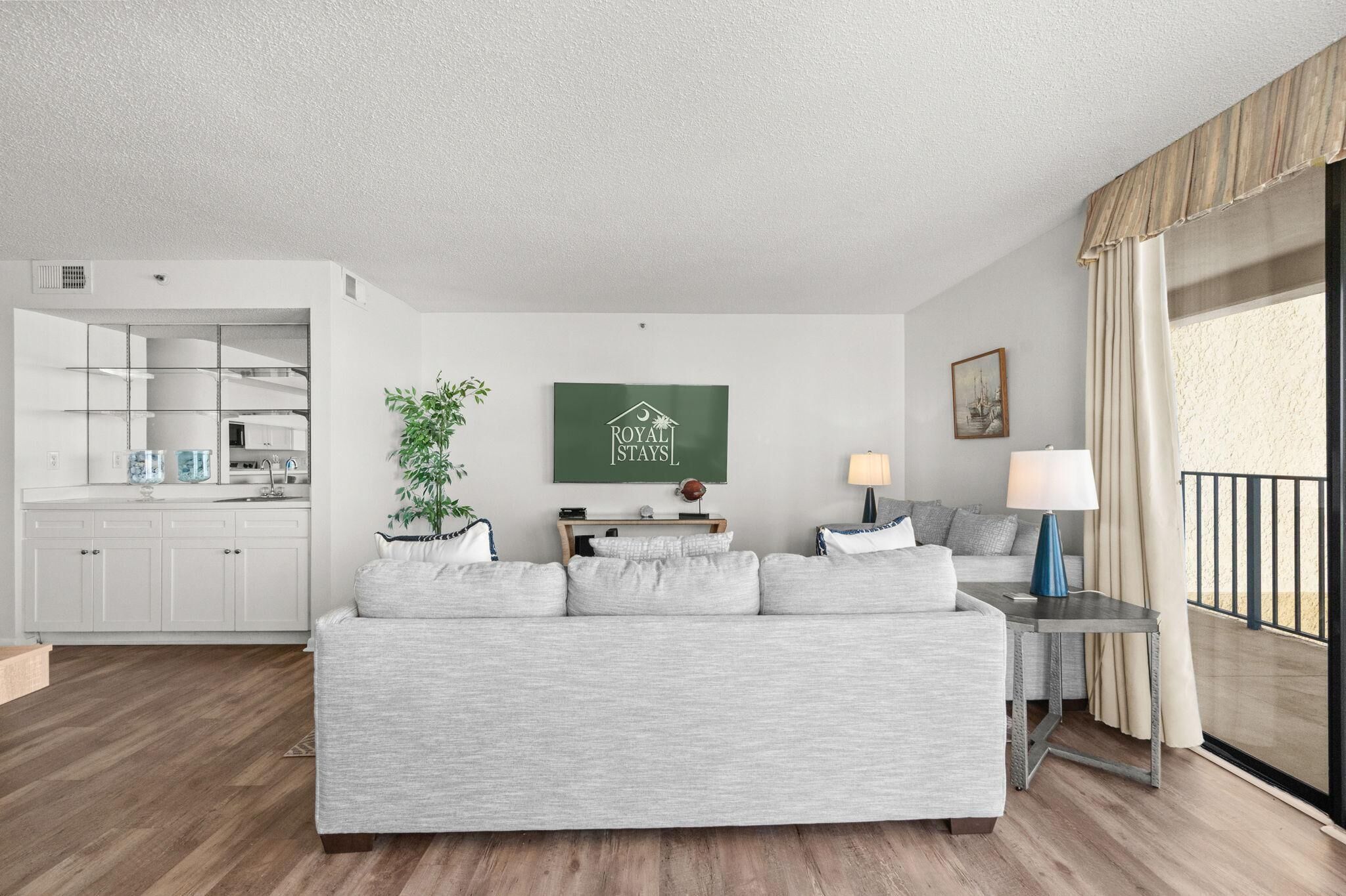 Ein modernes Wohnzimmer mit einer Couch, einem Essbereich, einer Küche und einem Balkon mit Vorhängen.