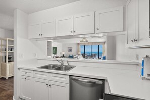 Una cocina moderna con muebles blancos, un lavamanos de acero inoxidable y lavavajillas.