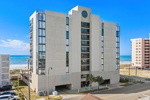 Un hotel de varios pisos con vista a la playa, un ventanal circular en el segundo piso y un letrero que dice 'Sea Castle'.