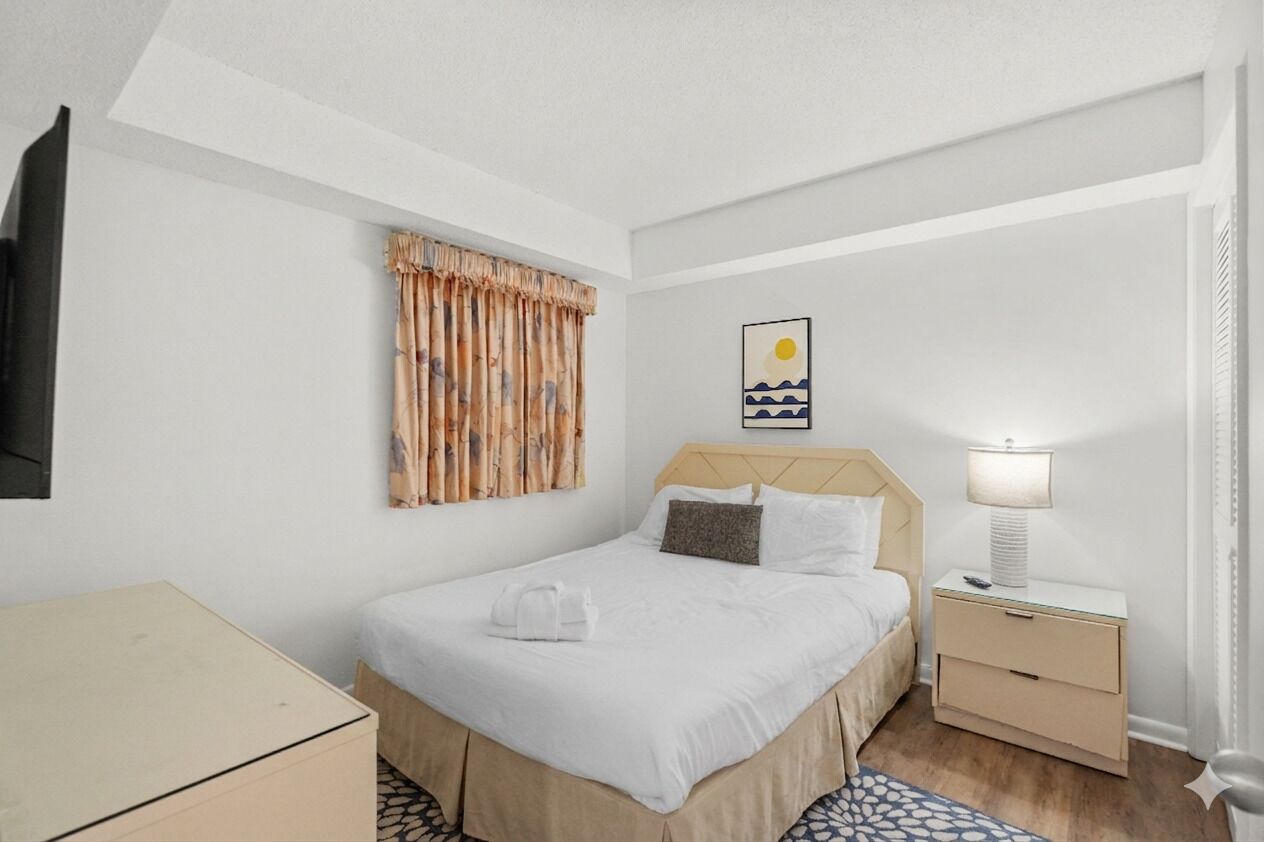 Una camera d'albergo con un letto, un comodino, una lampada e un quadro appeso al muro.