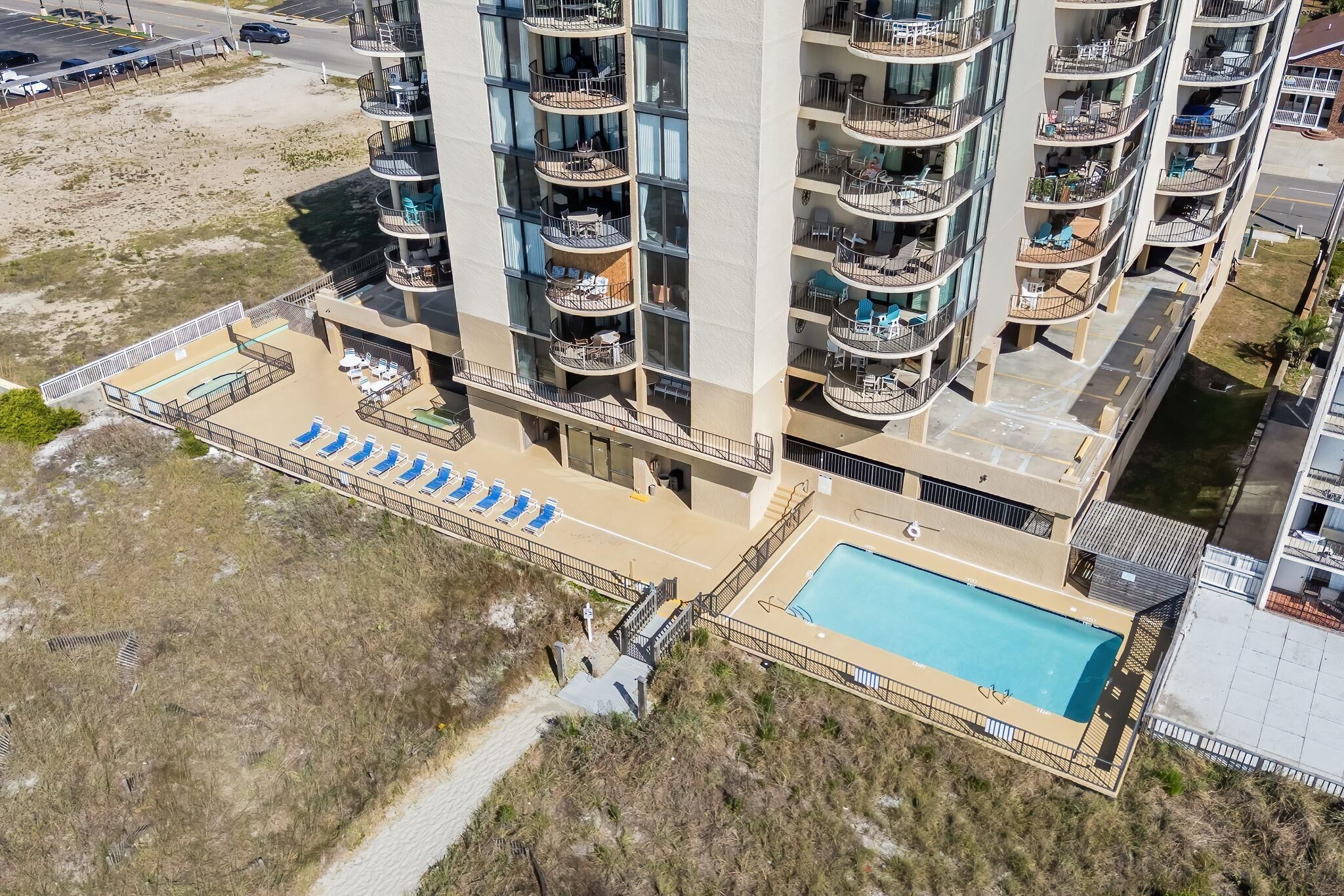 A high-rise building with multiple balconies, a swimming pool, and a beach area with sun loungers.