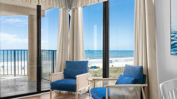 A room with large windows, a balcony, two blue chairs, and a view of the beach.