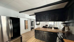 A modern kitchen with stainless steel appliances, dark cabinetry, and a wooden island.
