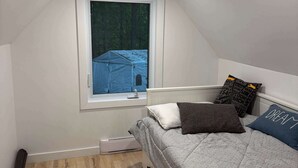 A small, triangular room with a bed, a window, and a view of a blue tent outside. - Waterfront Relaxation & Adventure | Albert (Pointe-Fortune)