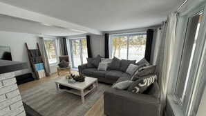 A modern living room with a sofa, coffee table, and a chair. There is a TV, a window with curtains, and a staircase.