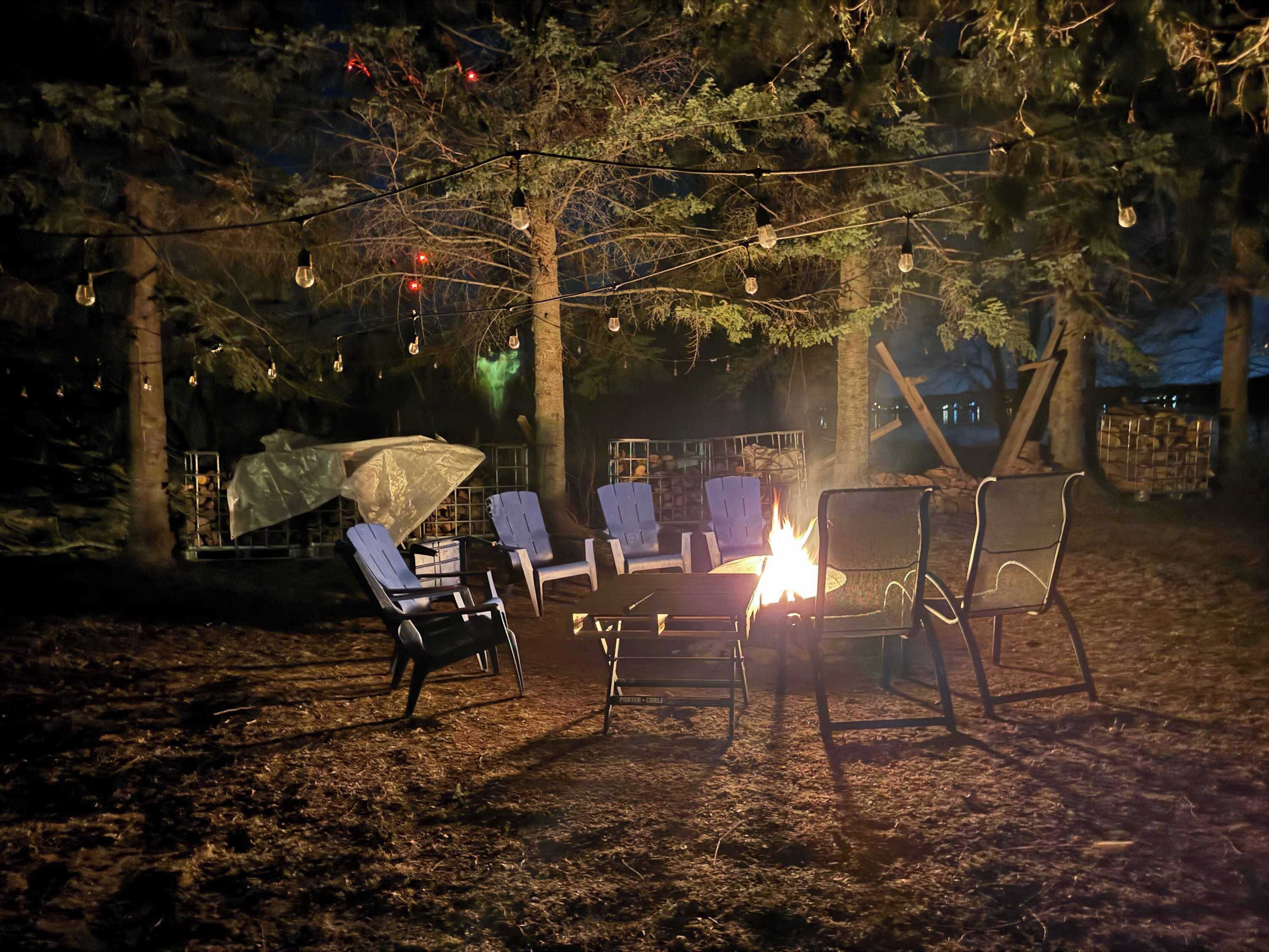 An outdoor seating area with chairs and a fire pit, surrounded by trees and string lights.