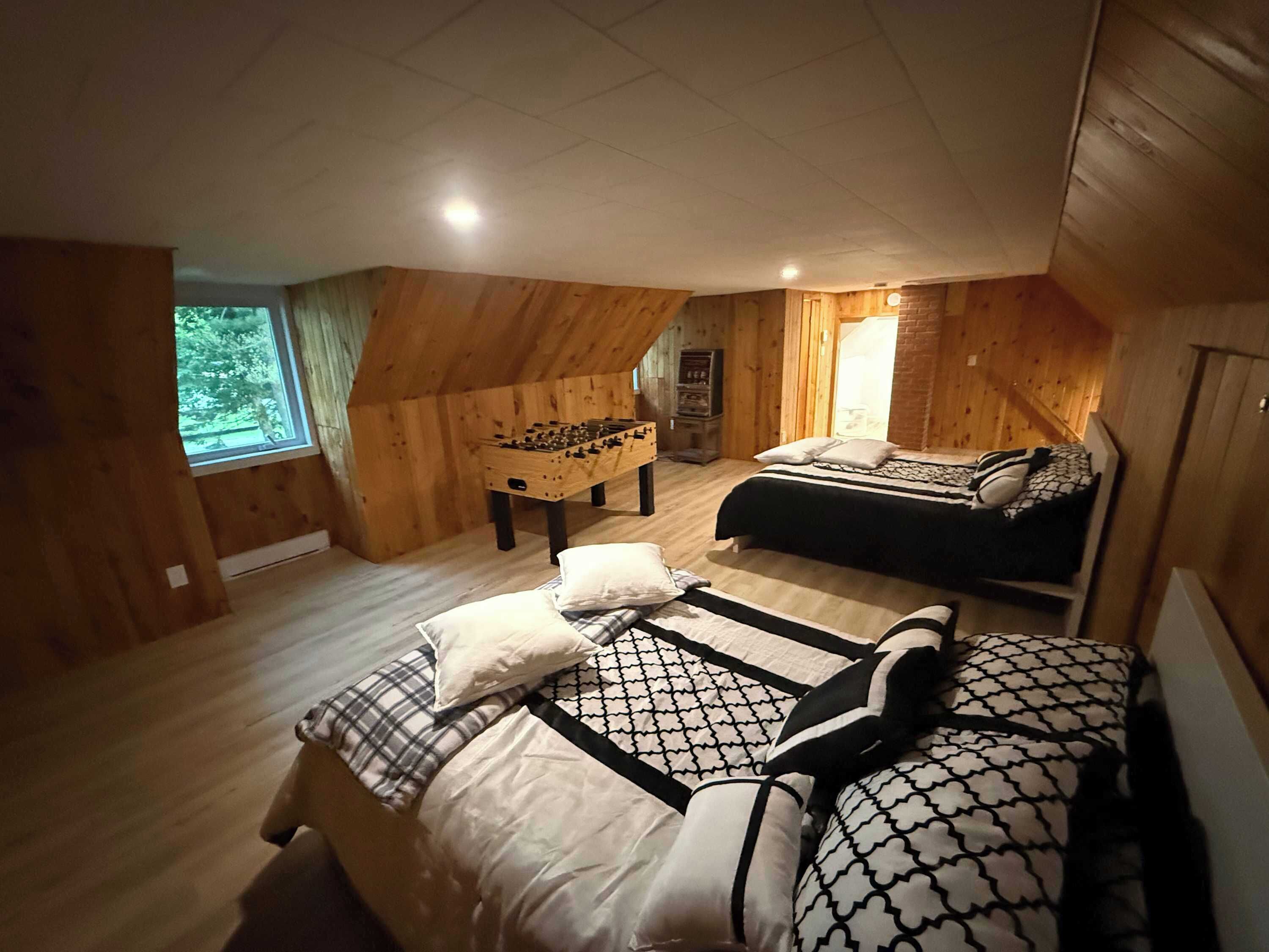 A cozy attic bedroom with a bed, a foosball table, and a window.