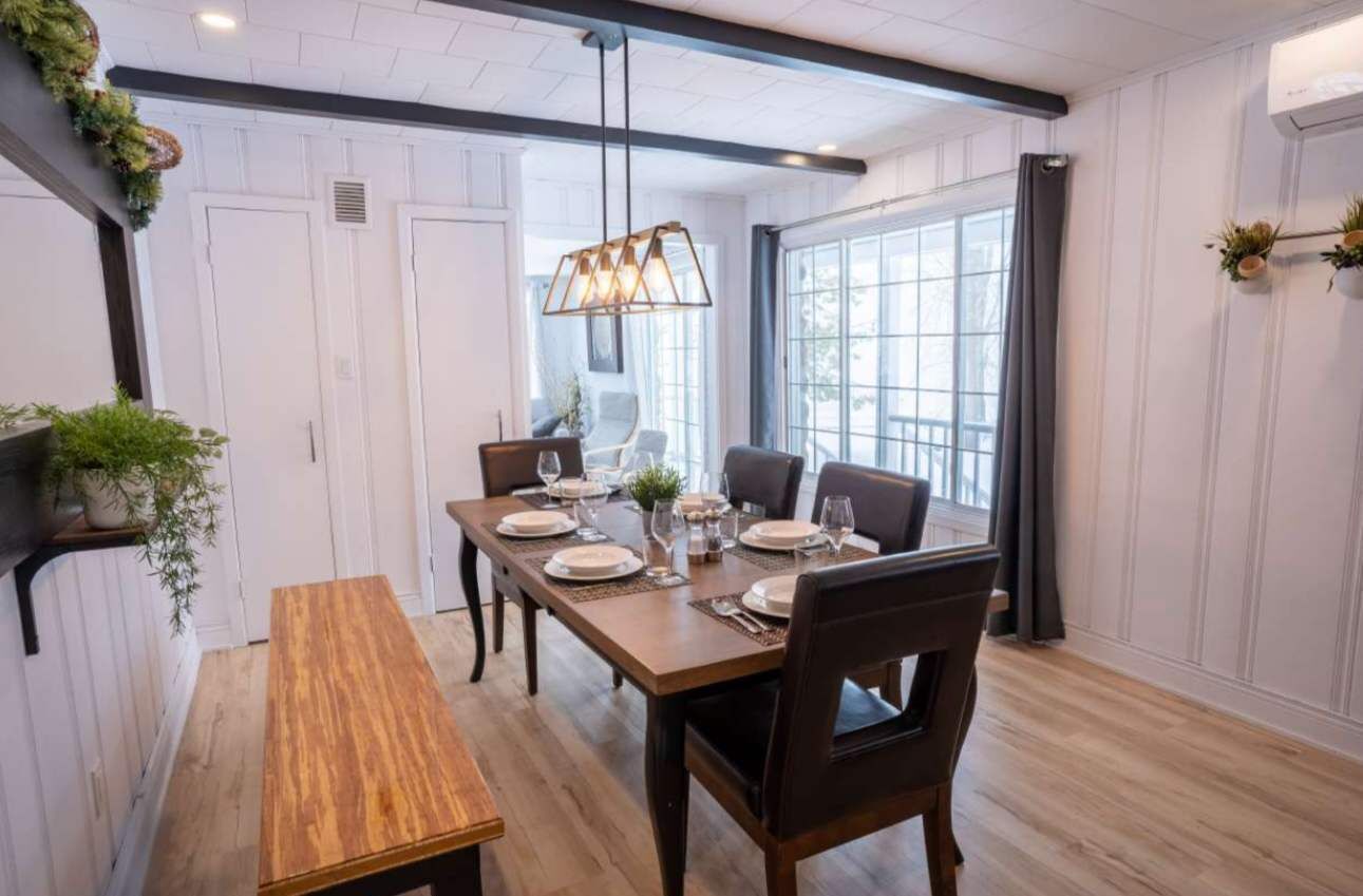 A dining area with a wooden table set for six, surrounded by chairs, with a hanging light fixture above.
