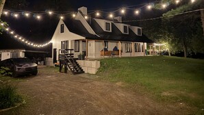 A two-story house with a covered porch, a car parked in front, and string lights overhead.