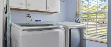 A laundry room with a washing machine and dryer, wooden flooring, a window with blinds, and white cabinets.