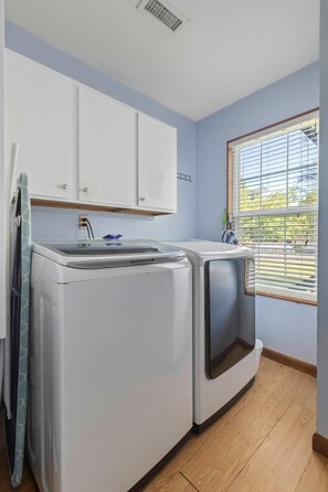 A laundry room with a washing machine and dryer, wooden flooring, a window with blinds, and white cabinets. - The Endless Summer-hot Tub-7 Beds (North Charleston)