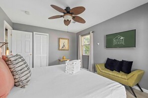 A hotel room with a bed, a yellow sofa, a ceiling fan, a framed picture, and a sign on the wall. - The Endless Summer-hot Tub-7 Beds (North Charleston)