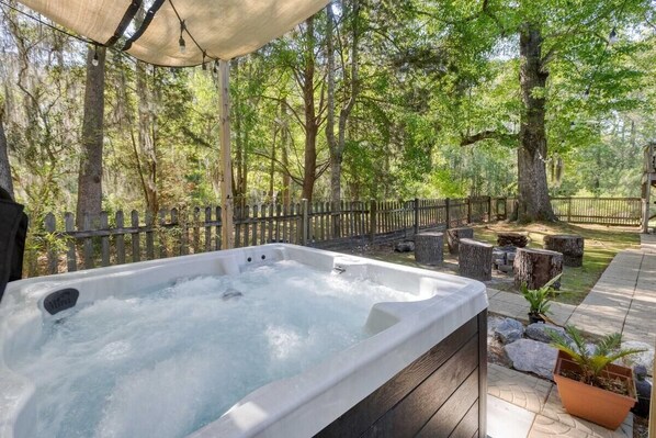 Ein Whirlpool in einer bewaldeten Außenanlage mit einer Holzterrasse, Steinbänken und einem Zaun.