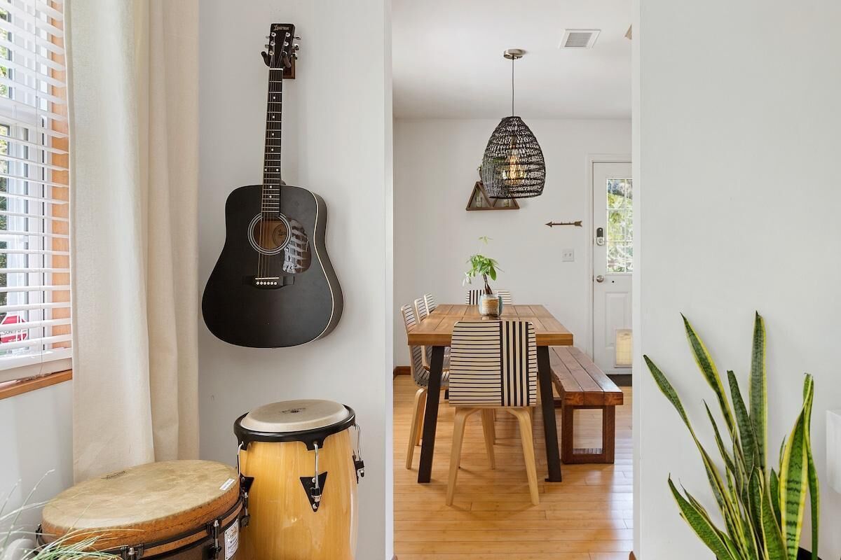 A room with a guitar, a drum, a dining table with chairs, and a hanging light fixture.