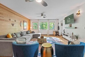 Ein modernes Wohnzimmer mit einer Holzwand, einem grauen Sofa, blauen Sesseln, einem Couchtisch und einem an der Wand montierten Fernseher.