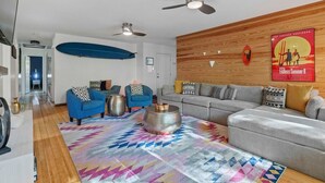 Un salon moderne avec un canapé gris, des fauteuils bleus, un tapis coloré et un mur d’accent en bois.