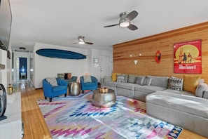 A modern living room with a grey sofa, blue armchairs, a colorful rug, and a wooden accent wall. - The Endless Summer-hot Tub-7 Beds (North Charleston)